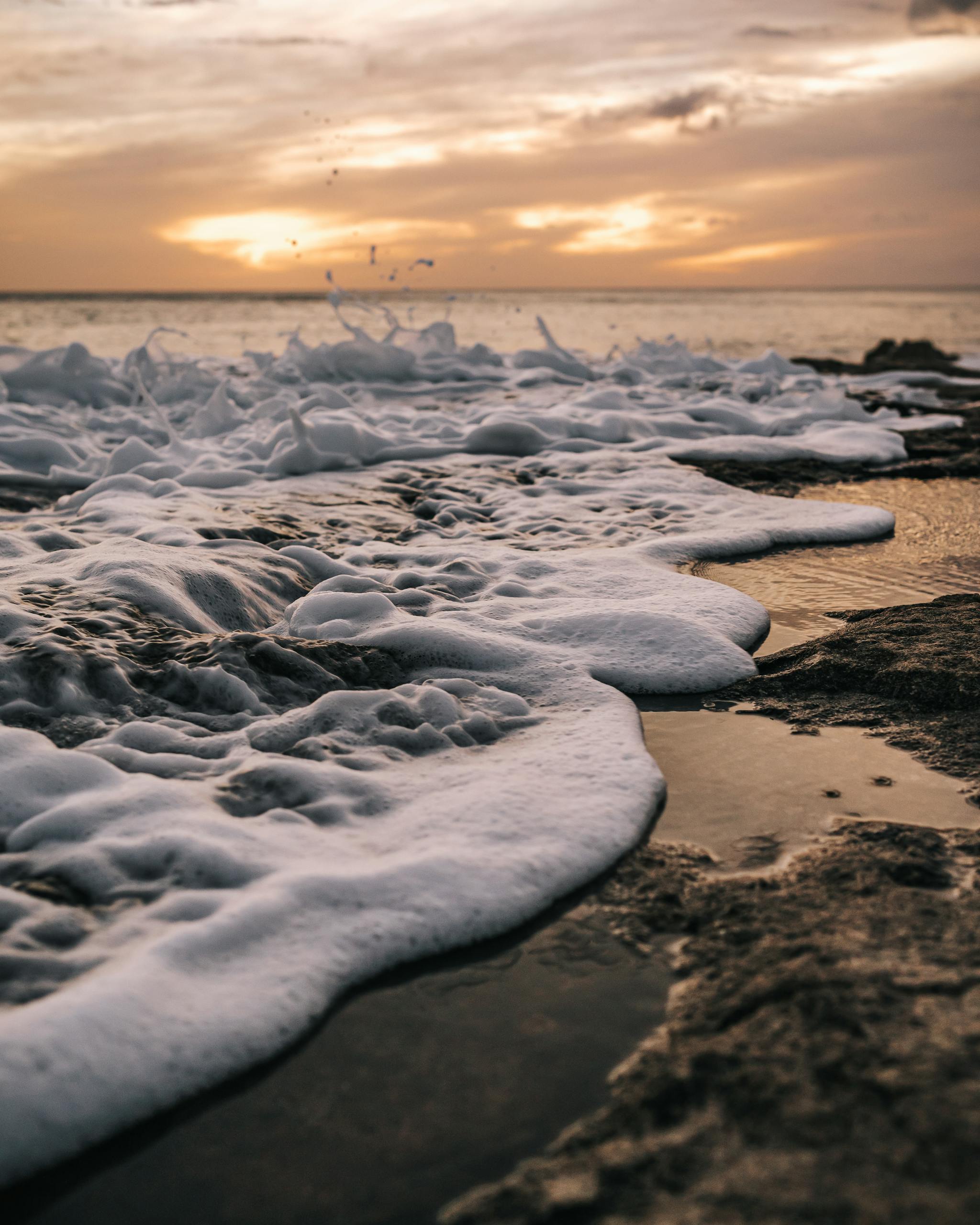 Discover the dramatic waves and foam at sunset on Waianae's rocky shore.